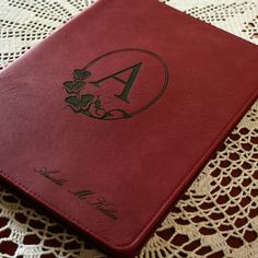 a red book sitting on top of a doily with a monogrammed letter