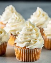 several cupcakes with white frosting sitting on a table