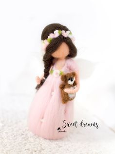 a small doll holding a teddy bear wearing a pink dress and flowered headband