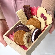 a person holding a wooden box filled with different types of cookies and pastries in it