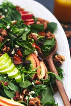 a salad with apples, spinach and walnuts on a white plate