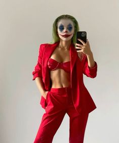 a woman dressed as the joker taking a selfie with her cell phone while standing in front of a white wall