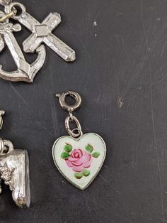 This listing is for 5 different silver tone charms. There is a pair of shoes, enameled heart, heart with rhinestone, anchor and cross. Three match and are on the same ring. The enameled heart is marked Wells Ster. The charms measure 15-20 mm long. They all have some wear including a few small chips of missing finish. R Vintage Metal Heart Charms, Vintage Metal Heart Charm, Silver Metal Heart Charm, Silver Heart Charm In Metal, Silver Heart Metal Charms, Silver Heart Charms With Dangling Details, Silver Heart Shaped Dangling Charms, Silver Heart-shaped Dangling Charms, Silver Enamel Heart Charm Jewelry