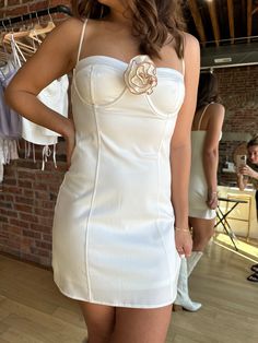 a woman standing in front of a brick wall wearing a white dress with flowers on it