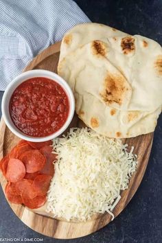 a wooden plate topped with pizza and cheese next to a bowl of sauce on top of it