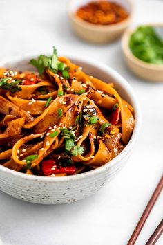 a white bowl filled with noodles and vegetables on top of a table next to chopsticks