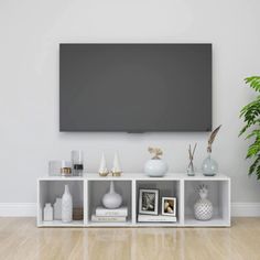 a tv mounted on the wall above some shelves with vases and other items in front of it