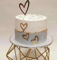 a white and blue cake with gold hearts on top sitting on a metal wire stand