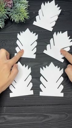 someone is making paper snowflakes out of white paper on a black table with pine branches