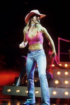 a woman in pink top and jeans on stage with lights around her neck, wearing cowboy hat