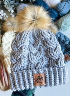 three knitted hats with pom - poms on top of each other next to yarn balls