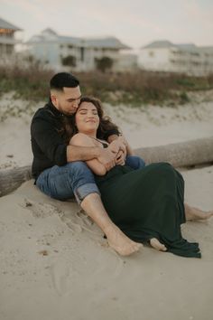 a man and woman sitting on the beach hugging