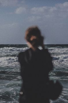 a blurry photo of a person standing in front of the ocean and looking at the waves