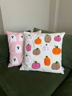 two decorative pillows on a green couch with ghost faces and pumpkins painted on them