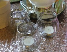 four clear glass candle holders sitting on top of a table next to a plate with silver sequins