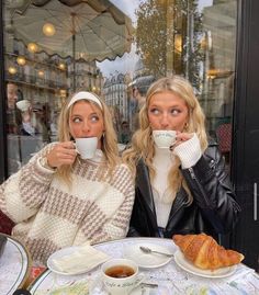 two women sitting at a table with cups of coffee and croissants in front of them