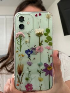 a woman holding up her phone case with flowers on it