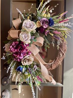 a wreath with flowers and ribbons hanging on a door