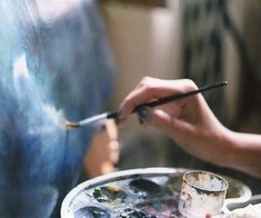 a person holding a brush and painting on an easel next to another person's hand