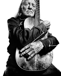 an old man is holding a guitar in his hands and looking at the camera with one hand