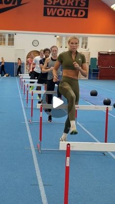 a group of people running over hurdles on a track in an indoor area with blue floors and orange walls