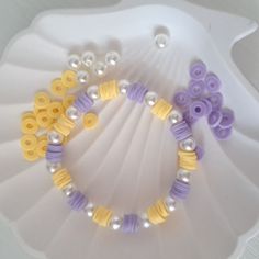 two bracelets with yellow and purple beads are on a white plate next to some pearls