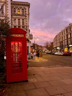 a red phone booth sitting on the side of a road next to tall buildings at dusk