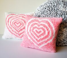 two pink and white pillows sitting next to each other on top of a table with the words radiating heart pillow