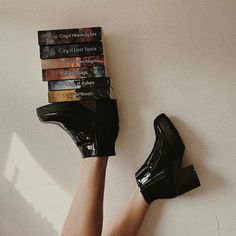 a woman's legs wearing high heeled black shoes with stacked books on them