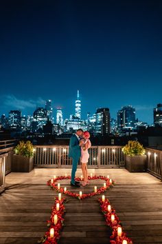 a man and woman standing on top of a wooden deck with candles in the shape of hearts