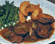 a white plate topped with green beans and meat covered in gravy next to potatoes