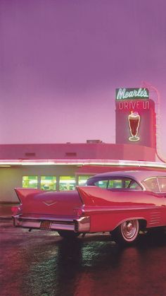 an old red car parked in front of a drive - in movie theater at night