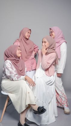 three women in hijabs are sitting on a chair and posing for the camera