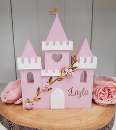 a pink princess castle cake with flowers on it's side and the name layla written in gold