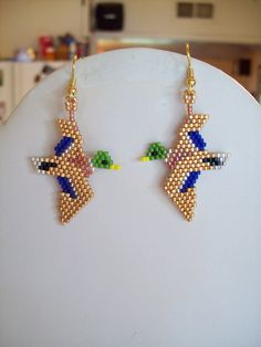 a pair of beaded cross earrings sitting on top of a white table next to a refrigerator