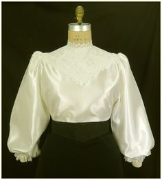 "Poly. Color: Antique White. Beautiful heavy weight bridal satin fabric with front lace yoke. Floral poly lace trim for collar, on elastic cuffs and front bodice. Lightly gathered full length bishop sleeves and button back closure. Generously cut for comfort. Machine washable. Circa 1898-1910. Made in U.S.A. Sizes: SM, MED, LG & XLG. Blouses ordered by bust measurement, inches: BUST SIZES 32\" - 34\" SMALL 35\" - 39\" MEDIUM 40\" - 44\" LARGE 45\" - 49\" XLARGE Blouses ordered by bust measuremen Victorian Blouse, Satin Blouses, White Satin, Antique White, Selling Jewelry, Lace Blouse, Satin Fabric, Heavy Weight, Womens Clothing Tops