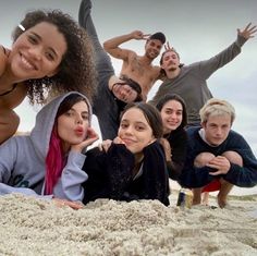 a group of people laying on top of a sandy beach next to the ocean with their arms in the air