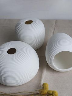 three white vases sitting on top of a table next to some yellow flowers and twine