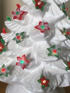 a white ceramic christmas tree with red and green flowers on it's base, sitting on a table