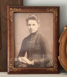 an old photo of a woman in dress sitting next to a clock on a shelf