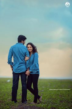 a man and woman are standing in the grass with their arms around each other, looking into the distance