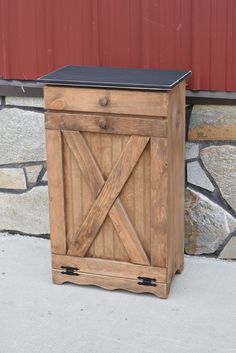 a small wooden cabinet sitting in front of a red building with a black top on it