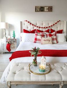 a white bed topped with red and white pillows sitting next to a christmas tree on top of a table