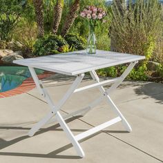 a white table sitting on top of a cement floor next to a pool and palm trees