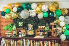 a table topped with lots of green and gold balloons next to a wall filled with desserts