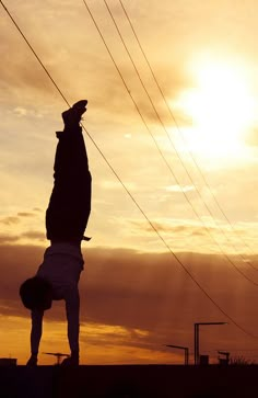 a person doing a handstand in front of the sun with power lines above