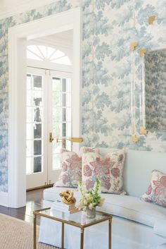 a living room with blue and white wallpaper, gold accents and a glass coffee table