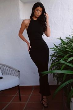 a woman in a black dress standing next to a potted plant