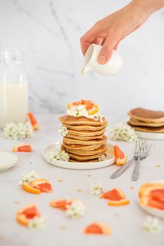 a person pouring syrup on top of a stack of pancakes with orange slices and flowers