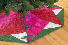 a quilted christmas tree skirt on top of a wooden floor next to a pine tree